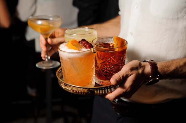 Man i tient un plateau avec des verres avec ambre Negroni et mélange jaune aigre