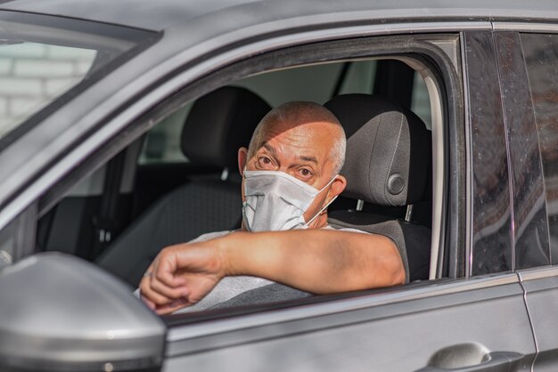 Man in masque médical conduisant une voiture, regardant la caméra.