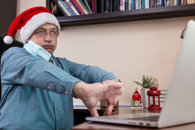 Man in santa claus hat parle à l'aide d'un ordinateur portable pour les amis et les enfants des appels vidéo. La salle est décorée de façon festive. Noël pendant le coronavirus.