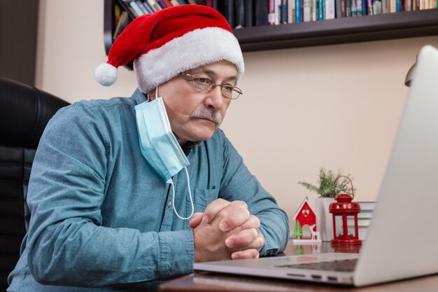 Man in santa claus hat parle à l'aide d'un ordinateur portable pour les amis et les enfants des appels vidéo. La salle est décorée de façon festive. Noël pendant le coronavirus.