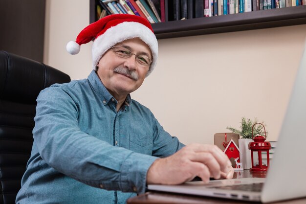 Man in santa claus hat parle à l'aide d'un ordinateur portable pour les amis et les enfants des appels vidéo. La salle est décorée de façon festive.