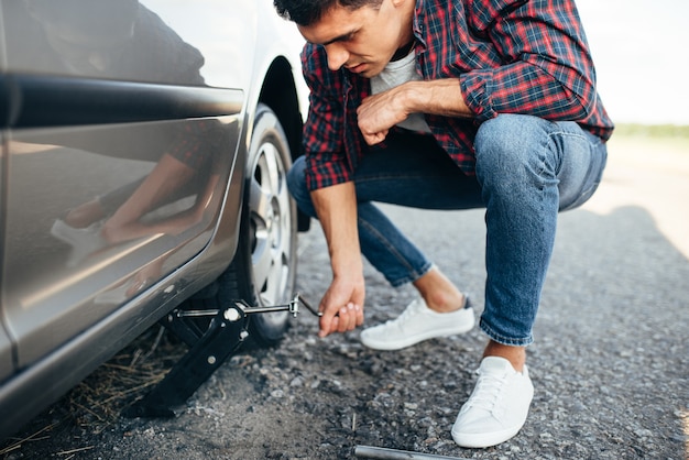 Man jack up voiture cassée, remplacement de roue. Véhicule avec pneu crevé sur le bord de la route