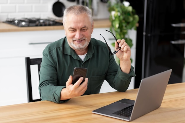 Man messagerie avec téléphone assis à la table dans la cuisine à domicile