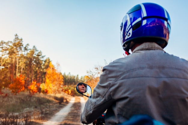 Man riding scooter sur route forestière d'automne. Conducteur en cyclomoteur casque. Vue arrière