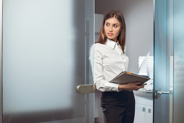 Manager femme debout au bureau au travail tenant des fichiers clip de documents tout en regardant sur le côté.