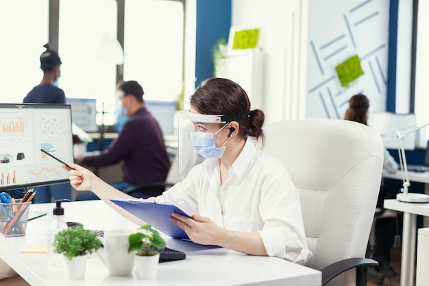 Manager portant une protection contre le covid 19 pendant la pandémie mondiale. Employés avec visières travaillant dans l'espace de travail de l'entreprise respectant la distance sociale analysant les données et les graphiques.