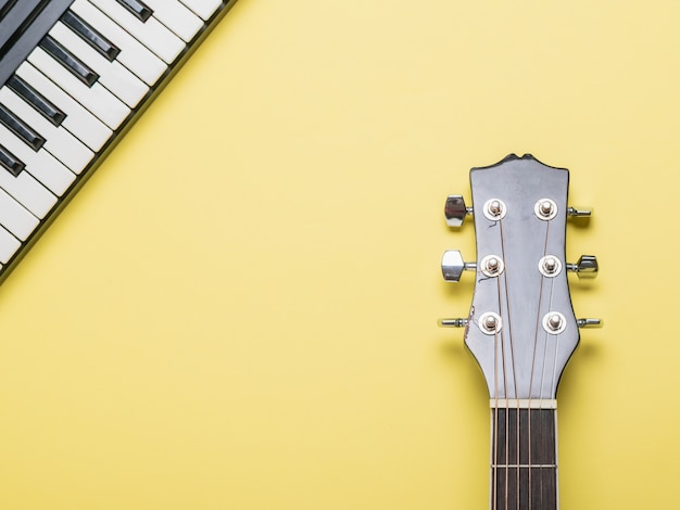 Manche de guitare acoustique et touches de piano sur une surface jaune