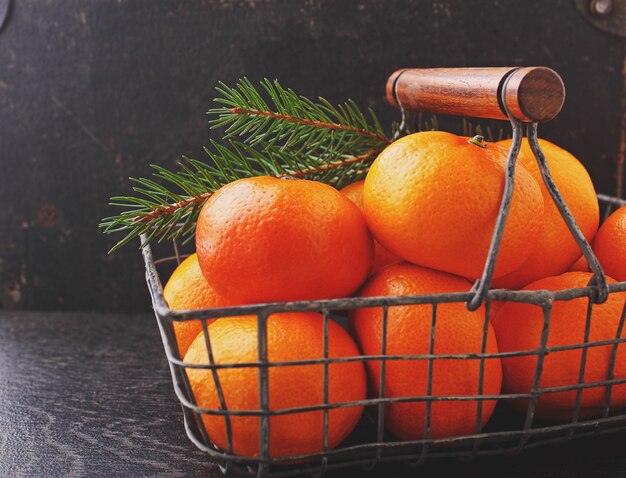 Mandarine dans un panier en métal avec une branche d&#39;un sapin de Noël sur fond noir