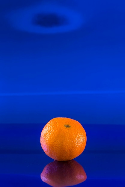 Une mandarine solitaire sur un fond bleu métallique et sur le dessus un trou noir