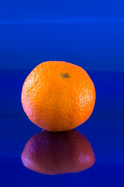 Une mandarine solitaire sur un fond bleu métallique