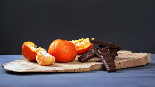 Mandarines au chocolat noir sur socle en bois sur fond gris foncé.