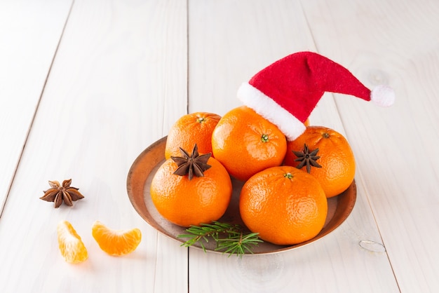 Mandarines avec chapeau de père Noël et anis sur une table en bois clair Noël et nouvel an