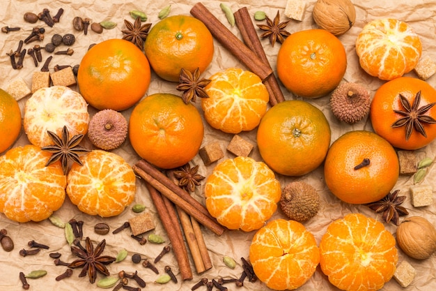 Mandarines et épices entières et pelées. Bâtons de cannelle, anis étoilé, piment de la Jamaïque et cardamome, litchi et noix. Fond de papier brun. Mise à plat