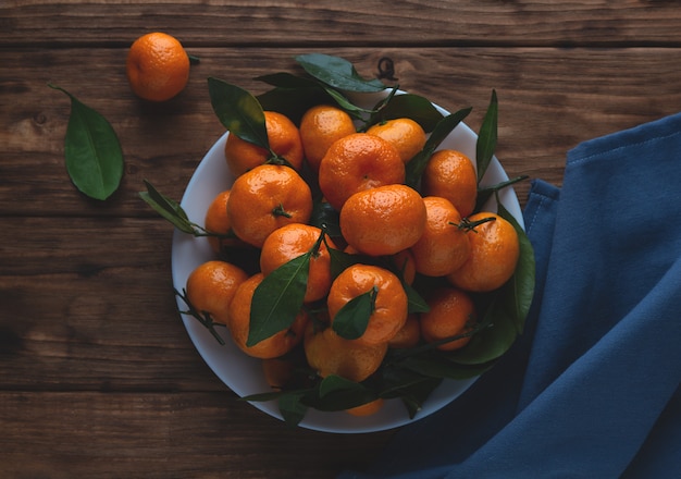 Mandarines avec des feuilles dans une assiette sur un fond en bois.