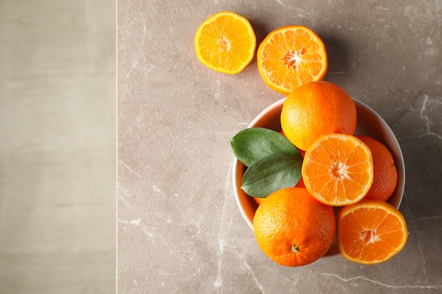 Mandarines et feuilles dans un bol sur une table grise, vue du dessus