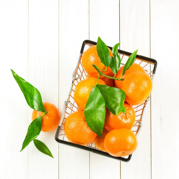 Mandarines avec des feuilles dans le panier sur une table en bois blanche. Vue de dessus