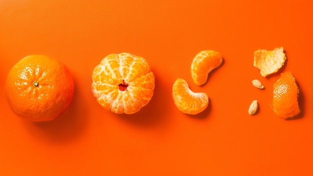 Les mandarines sur fond orange en quartiers pelés entiers et peler la bannière à plat