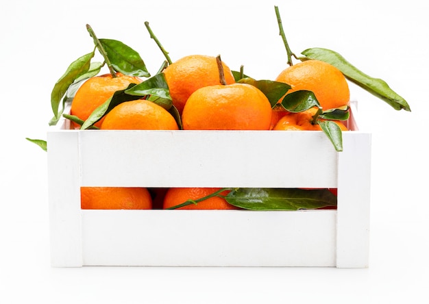 Mandarines fraîches et crues avec des feuilles vertes dans une boîte en bois