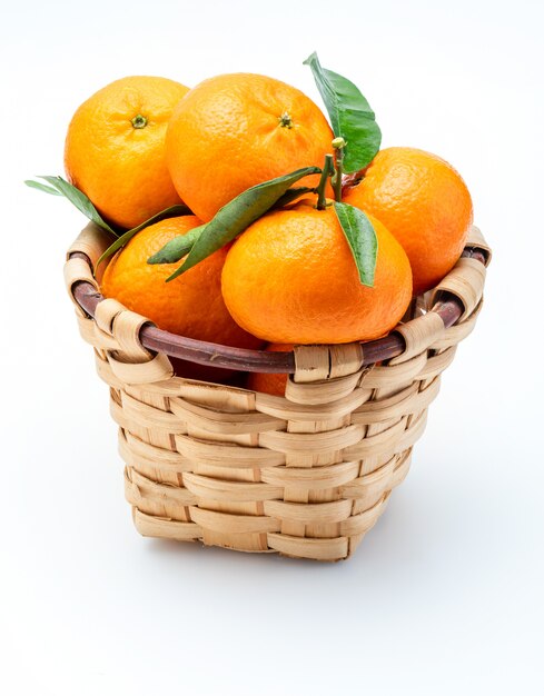 Mandarines fraîches et crues avec des feuilles vertes dans un panier en osier rustique.