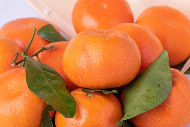 Mandarines fraîches, mandarines, avec des feuilles, dans une corbeille en bois retournée avec une surface blanche.