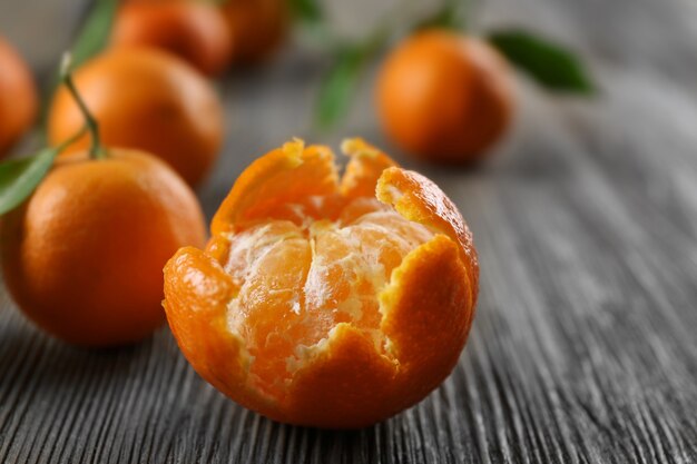 Mandarines fraîches pelées avec des feuilles et des mandarines mûres sur table en bois, gros plan