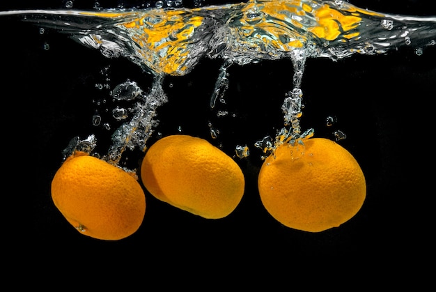 Les mandarines fraîches sont tombées dans l'eau avec des bulles sur fond noir