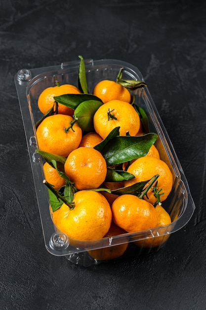 Mandarines, mandarines dans un récipient en plastique, boîte. Fond noir. Vue de dessus