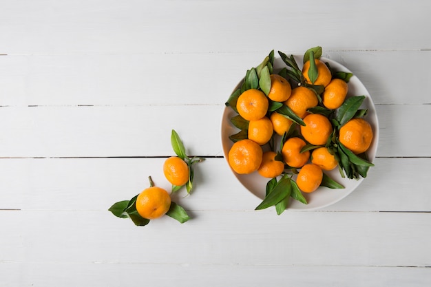 Mandarines mandarines avec des feuilles dans une plaque blanche sur fond de bois blanc. Vue de dessus, espace copie.