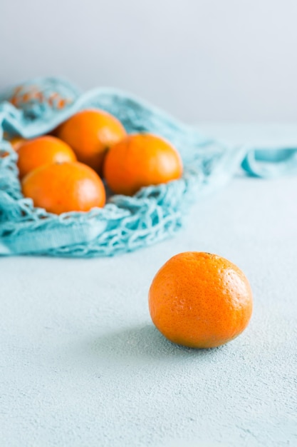 Mandarines mûres dans un sac en filet sur fond bleu. Fruits dans un emballage durable. Vue verticale