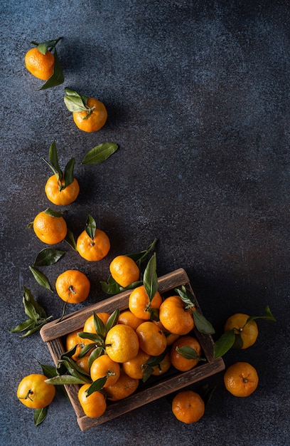 Mandarines mûres avec des feuilles dans une boîte en bois, vue du dessus