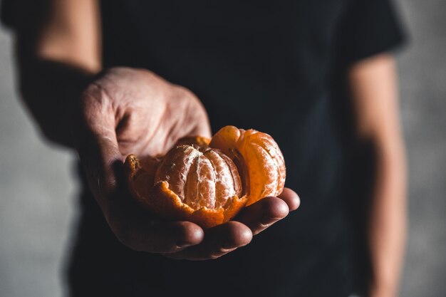 Mandarines orange douce juteuse mûre dans une main humaine sur un fond sombre. PNOV2019