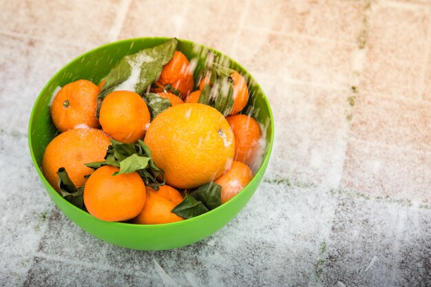 Mandarines et oranges dans le bol vert sur la neige Il se dresse dans la rue Feuilles vertes fanées de