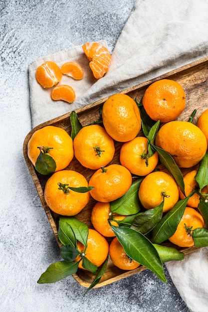 Mandarines (oranges, mandarines, clémentines, agrumes) avec des feuilles dans un bol en bois. Fond gris. Vue de dessus