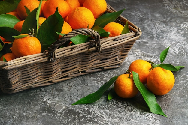 Mandarines (oranges, mandarines, clémentines, agrumes) avec des feuilles dans un panier en bois sur fond de ciment gris. Nourriture végétarienne biologique. Fruits locaux d'hiver. Concept d'alimentation saine de désintoxication.