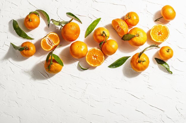 Mandarines (oranges, mandarines, clémentines, agrumes) à feuilles vertes. Lumière dure moderne, ombre sombre. Fond de mastic blanc, mise à plat créative, vue de dessus