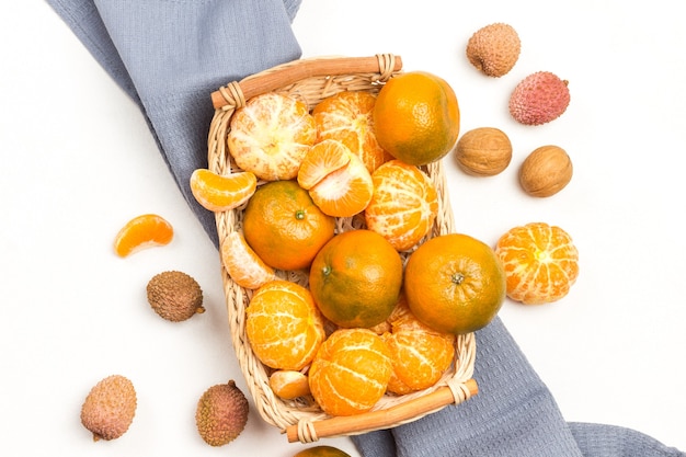 Mandarines en panier en osier sur serviette grise. Baies de litchi sur table. Fond blanc. Copiez l'espace. Mise à plat