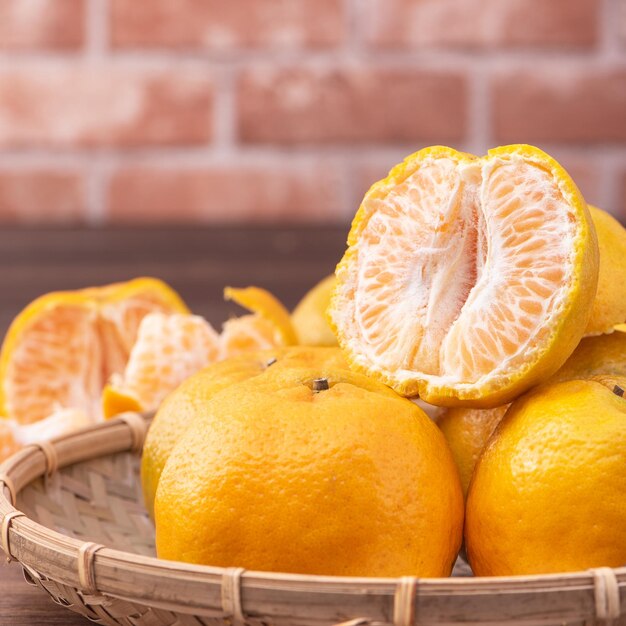 Mandarines pelées dans un panier de tamis en bambou sur une table en bois sombre avec fond de mur de briques rouges Concept de design de fruits du nouvel an lunaire chinois gros plan