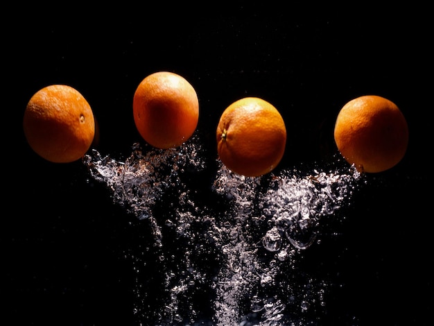 Mandarines tombant dans l'eau avec éclaboussures sur fond noir