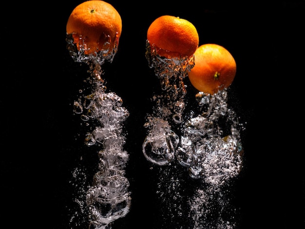 Mandarines tombant dans l'eau avec éclaboussures sur fond noir