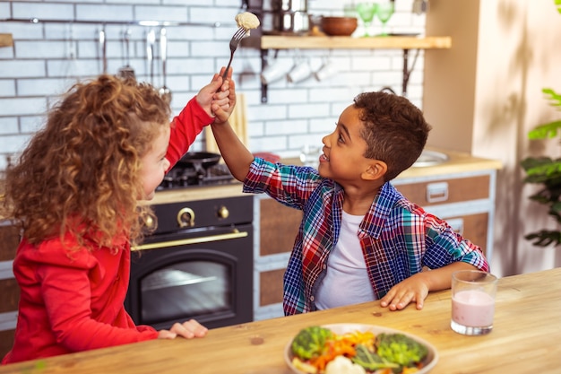 Mange le. Enfant joyeux assis près de son ami et s'amusant au dîner