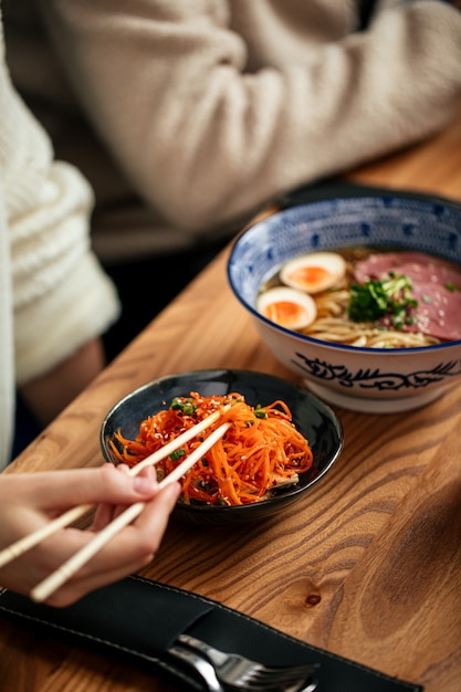 Manger des carottes marinées asiatiques et des ramen shoyu avec des baguettes