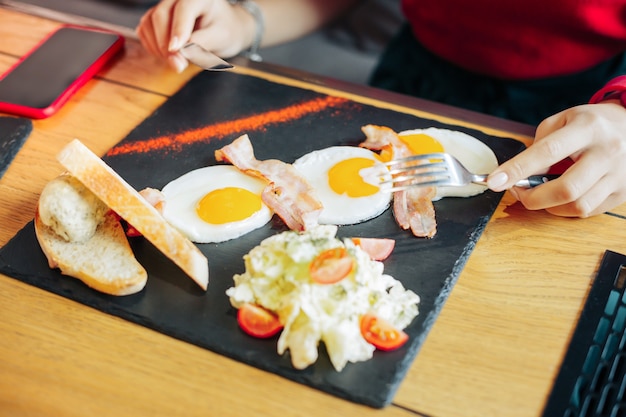 Manger des œufs au plat. Vue de dessus d'une femme mangeant de délicieux œufs au plat avec du bacon et de la salade