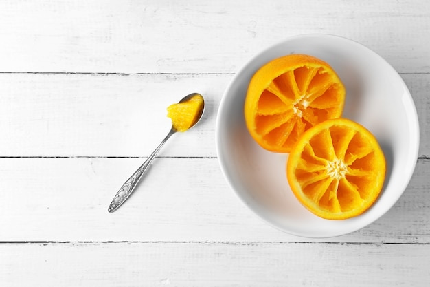 Manger des oranges avec une cuillère sur une table en bois blanc