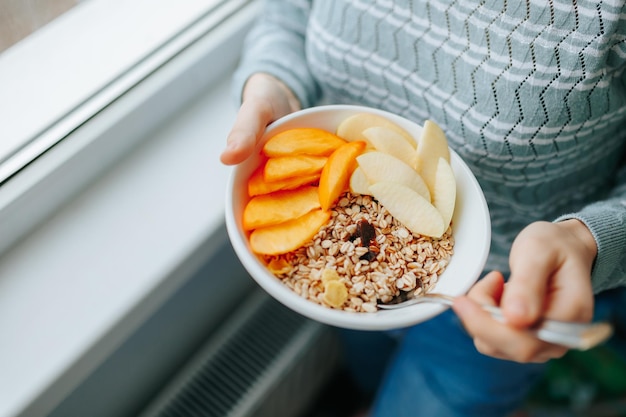 Manger un petit-déjeuner sain muesli bol et fruits frais dans un bol en céramique dans les mains de la femme manger propre di