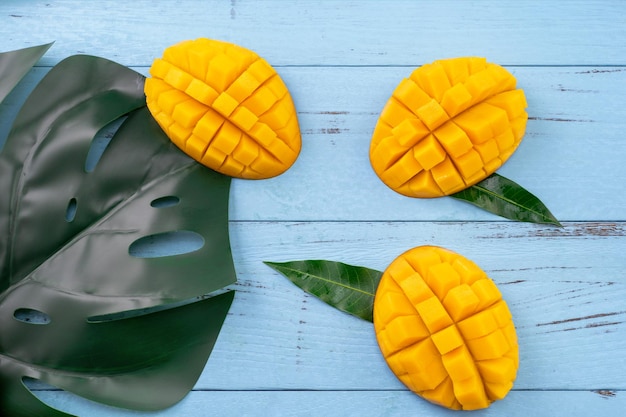 Mangue fraîche beau fruit haché avec des feuilles vertes sur fond de bois bleu vif Concept de design de fruits tropicaux Mise à plat Vue de dessus Copier l'espace