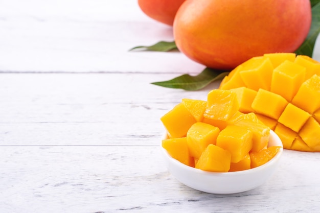 Mangue fraîche, beaux fruits hachés avec des feuilles vertes sur une table en bois clair