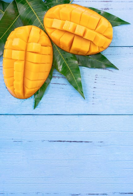 Photo mangue fraîche hachée avec des feuilles vertes sur fond de bois de couleur bleu vif au-dessus de la vue de dessus de l'espace de copie à plat en gros plan concept de fruits tropicaux