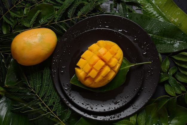 Mangue fraîche avec des morceaux de mangue en dés sur une assiette ou sur des feuilles en arrière-plan