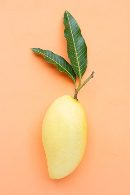 Mangue jaune sur surface orange, fruits tropicaux juteux et sucrés.