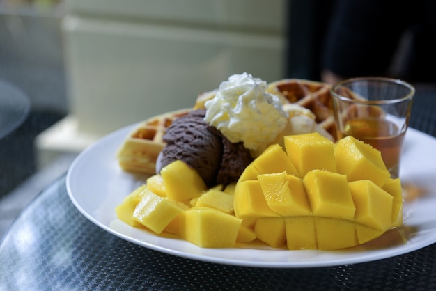 Mangue mûre, crème glacée, gaufres et miel dans un plat blanc.